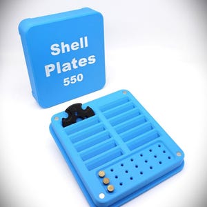 May include: A light blue shell plate organizer with the text "Shell Plates 550" on the lid. The open organizer has multiple compartments, a black tool, and brass-colored pins. The text "Shellplate and Locator Pins Not Included" is at the top.
