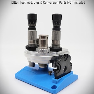 Könnte beinhalten: Ein Wiederlade-Werkzeugkopf mit zwei schwarzen Zifferblättern und silbernen Metallkomponenten. Der Werkzeugkopf ist auf einer blauen Basis montiert. Der Text "Dillon Toolhead, Dies & Conversion Parts NOT Included" steht oben.