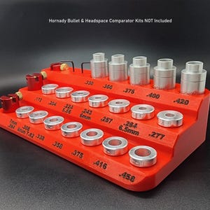 Könnte beinhalten: Ein roter Plastik-Organizer mit mehreren Reihen silberner Ringe. Die Ringe sind mit verschiedenen Maßen in Zoll und Millimetern beschriftet. Der Organizer ist mit "Hornady Bullet & Headspace Comparator Kits NOT included" beschriftet.