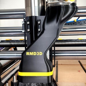 Könnte beinhalten: Ein schwarzer und gelber CNC-Maschinen-Staubschutz mit dem Text "RMD3D". Der Staubschutz hat eine Bürste an der Unterseite und ist an einer Metall- und Kunststoffmaschine befestigt. Die Maschine steht auf einer Holzoberfläche.