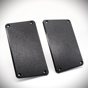 Puede incluir: Dos placas rectangulares negras con una superficie texturizada. Las placas tienen esquinas redondeadas y están ligeramente inclinadas.