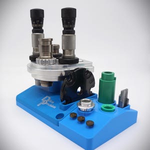 May include: A blue reloading press with a black dial and a green accessory holder. The press is labelled "Blue Precision".
