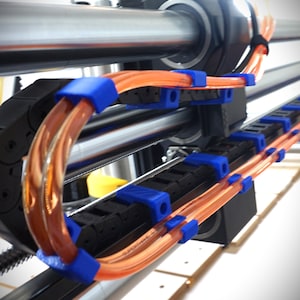 Puede incluir: Primer plano de una cadena de cables negra con tubos naranja y azul que la atraviesan. La cadena de cables está unida a una varilla de metal plateado.