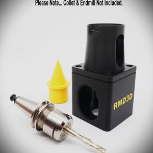Puede incluir: Un soporte de herramienta negro impreso en 3D con el texto amarillo RMD3D, una tapa cónica de plástico amarilla y una pinza de metal plateado con una fresa. El texto Please Note... Collet & Endmill Not Included es visible arriba.