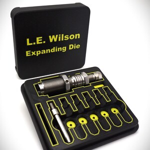 Może przedstawiać: Czarne plastikowe pudełko z żółtą etykietą z napisem "L.E. Wilson Expanding Die". Pudełko jest otwarte i zawiera srebrną matrycę rozprężającą i zestaw małych, czarnych plastikowych wstawek z żółtą obwódką.