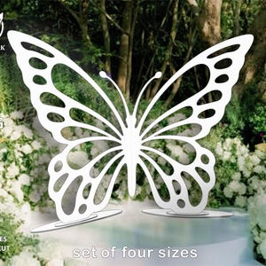 May include: A set of four sizes of white butterfly cutouts, designed for laser cutting. The butterflies are shown against a background of green foliage and white flowers.