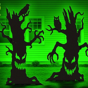 May include: Black metal Halloween yard decorations featuring spooky trees with carved faces and outstretched branches. One tree has a raven perched on a branch, the other an owl. The background is a green lawn and house.