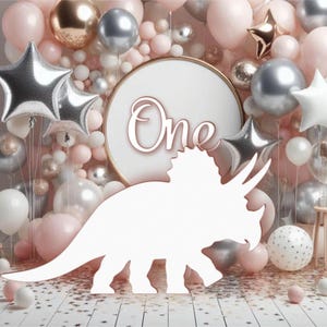 May include: White dinosaur cutout with the word "One" in gold lettering on a white circle background. The background is decorated with pink, white, and silver balloons.