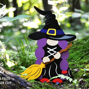 May include: A purple and black witch gnome holding a broom with a yellow bristle. The gnome is wearing a black hat with a blue band and a yellow buckle. The gnome is standing on a bed of green moss.