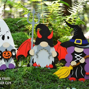 May include: Three Halloween gnomes, one dressed as a ghost holding a jack-o-lantern, one dressed as a devil with red wings and a trident, and one dressed as a witch with a purple hat and a broom.