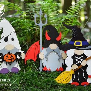 May include: Three Halloween gnomes, one dressed as a ghost holding a pumpkin and "BOO" sign, one dressed as a devil with red wings and a trident, and one dressed as a witch with a black hat and broom.