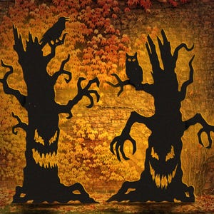 May include: Two black silhouette tree cutouts with jagged, glowing yellow eyes and mouths. The left tree features a perched raven, while the right tree displays an owl on a branch. Both trees have twisted, claw-like branches and roots.