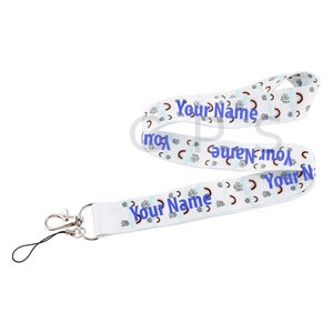 Puede incluir: Lanyard blanco con un patrón geométrico azul y negro. El lanyard tiene un clip giratorio plateado y un anillo de teléfono desmontable. El texto "Your Name" está impreso en el lanyard en azul.