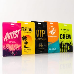 May include: Five rectangular plastic event passes with lanyard slots. The first is pink with "ARTIST" text, the second yellow with "FESTIVAL SPONSOR" and palm trees, the third black with "VIP BACKSTAGE", the fourth orange and blue with "ISLAND VIBES", and the fifth lime green with "CREW" and a sound wave graphic.