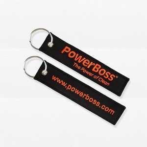 Könnte beinhalten: Zwei schwarze Schlüsselanhänger mit orangefarbenem gesticktem Text. Der obere Schlüsselanhänger lautet "PowerBOSS The Power of Clean". Der untere Schlüsselanhänger lautet "www.powerboss.com". Jeder Schlüsselanhänger hat einen silbernen Metallring.