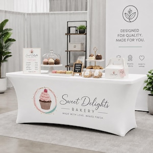 May include: A white rectangular fitted tablecloth featuring a printed logo for Sweet Delights Bakery, which includes a pink cupcake illustration and the text "Sweet Delights BAKERY MADE WITH LOVE. BAKED FRESH." The cover has a smooth, stretch fabric.