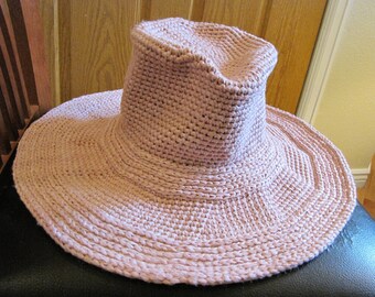 May include: A wide-brimmed sun hat in a pale pink color, crocheted with a textured pattern. The hat has a slightly rounded crown and a wide, floppy brim.