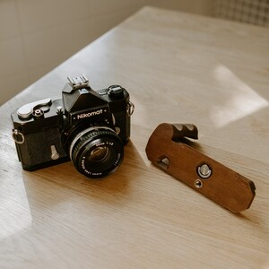 May include: A black Nikon Nikomat camera with a 50mm lens and a wooden hand grip.
