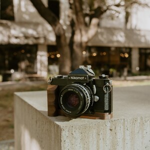 May include: A black Nikon Nikomat camera with a 50mm 1:1.8 lens, sitting on a concrete surface.