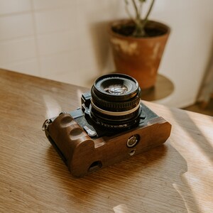 May include: A black camera with a wooden grip and a silver lens. The camera is sitting on a wooden table.