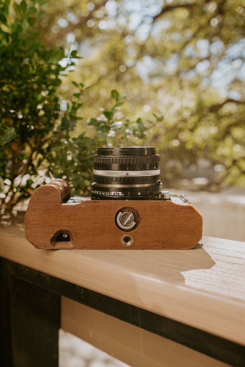 May include: A vintage camera with a wooden body and a black lens. The camera is sitting on a wooden surface.
