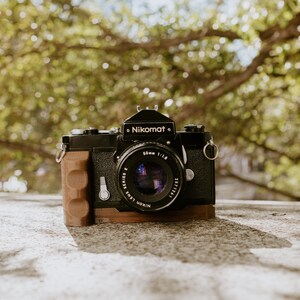 May include: A black Nikon Nikomat camera with a 50mm f/1.8 lens. The camera has a brown leather grip and a silver strap.