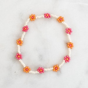 Peut inclure: Un bracelet en perles blanches avec des perles en forme de fleurs roses et orange.