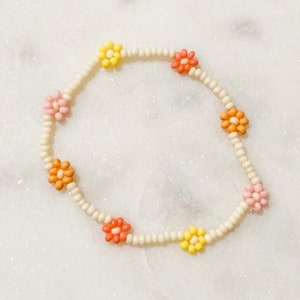 May include: A white beaded bracelet with colorful flower-shaped beads. The beads are pink, yellow, and orange.