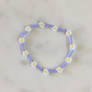 May include: A purple beaded bracelet with white daisy flower accents.