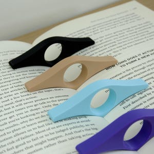 Peut inclure: Quatre marque-pages de couleurs différentes pour livres. Les marque-pages sont en plastique et ont la forme d'un doigt courbé. Les couleurs sont noir, beige, bleu clair et violet.