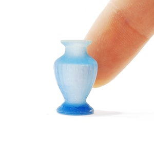 May include: A small, light blue glass vase with a rounded base and a narrow neck. The vase is made of frosted glass and has a slightly textured surface.