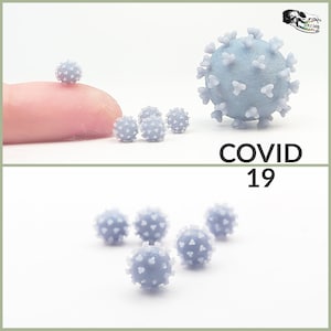May include: A set of small, gray, 3D printed models of the COVID-19 virus. The models are different sizes, with the largest one being about the size of a fingertip. The models are on a white background. COVID 19 is written in black text below the models.