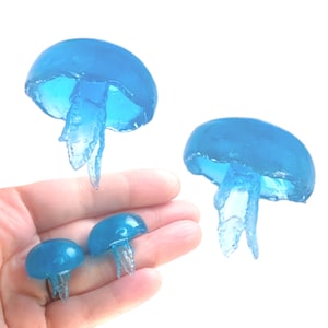 May include: Four blue jellyfish made of resin, two are small and two are large. The larger jellyfish are suspended in mid-air, while the smaller jellyfish are held in a hand.