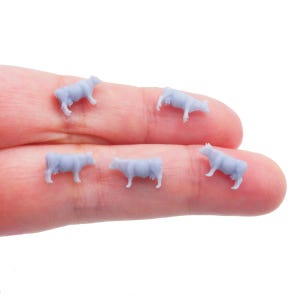 Può includere: Cinque piccole statuette di mucche azzurre. Le mucche in miniatura sono in varie pose, alcune in piedi e altre che sembrano brucare. Questi minuscoli modelli di animali da fattoria sono probabilmente per un plastico ferroviario o un diorama.