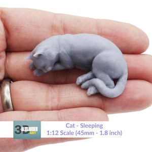 Op de afbeelding: Een grijs, 3D-geprint model van een slapende kat. Het model is 45 mm lang en is op schaal 1:12.