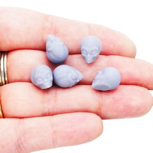 Può includere: Una collezione di piccole statuette a forma di testa di alieno azzurro chiaro. Le sculture dettagliate presentano grandi occhi e una consistenza liscia. Le statuette sono tenute in una mano, mostrando le loro dimensioni e il loro design. Queste mini teste aliene sono ideali per l'artigianato o la collezione.