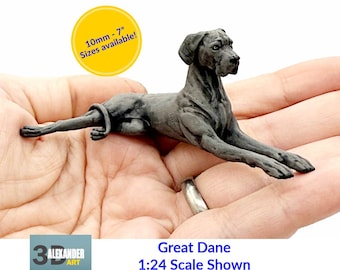 May include: A detailed grey Great Dane figurine in a resting position. The image includes the text "10mm - 7" Sizes available!" in a yellow circle. The text "Great Dane 1:24 Scale Shown" is also visible.