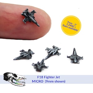 May include: Miniature F18 Fighter Jet models in a dark metallic finish. The image shows several small airplane models, with one held on a fingertip. Text on the image reads "F18 Fighter Jet MICRO (9mm shown)" and "7mm - 1" Sizes available!"