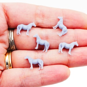 May include: Five small, light blue horse figurines in various poses. The miniature horses are standing, rearing, and walking. The figurines are held in a person's hand, with rings visible on the fingers.