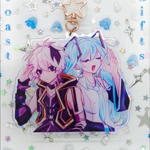 Pode incluir: Um chaveiro de acr&iacute;lico com uma ilustra&ccedil;&atilde;o estilo anime de dois personagens, um com cabelo curto rosa e colete escuro, o outro com cabelo longo azul claro. O chaveiro tem um fecho em forma de estrela e o texto Strawbunny Toast Gifts.