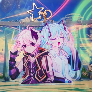 Pode incluir: Um porta-chaves de acr&iacute;lico transparente com um fecho em forma de estrela e uma ilustra&ccedil;&atilde;o impressa de duas personagens de estilo anime. Uma personagem tem cabelo branco curto com detalhes escuros e a outra tem cabelo comprido azul-claro.