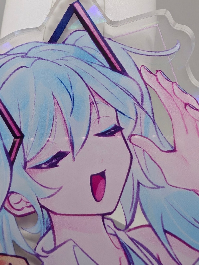 Pode incluir: Um expositor de acr&iacute;lico transparente com uma ilustra&ccedil;&atilde;o impressa de uma personagem com cabelo azul claro, olhos fechados e boca aberta. A personagem tem contornos roxos escuros e usa um acess&oacute;rio de cabelo triangular roxo escuro.