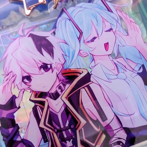 Pode incluir: Um porta-chaves de acr&iacute;lico transparente com uma ilustra&ccedil;&atilde;o impressa de duas personagens de estilo anime. Uma personagem tem cabelo branco curto e um traje preto e roxo, enquanto a outra tem cabelo comprido azul claro. Inclui um fecho em forma de estrela em ouro rosa.
