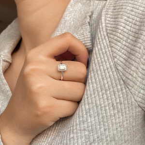 May include: A silver ring featuring a clear, rectangular gemstone set in a halo of smaller stones.