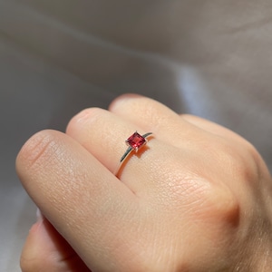 May include: A silver ring with a small, square, red gemstone.