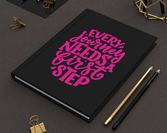 May include: Black notebook with the text "Every journey needs a first step" in pink lettering.