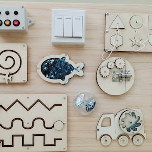 May include: A wooden activity board with various textures and activities for children. It features a light switch, a zipper, a lock with gears, a maze, a shape sorter, a spinning wheel, and a fish with sequins.