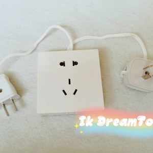 Puede incluir: Adaptador eléctrico blanco con un cable blanco y dos clavijas. El adaptador tiene una toma de corriente de tres clavijas y un enchufe redondo de tres clavijas.