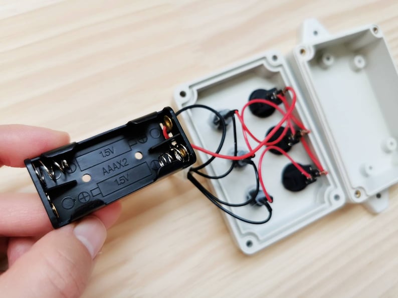 May include: A black battery pack with two AAA batteries and the text "1.5V AAAx2 1.5V" printed on it. The battery pack is connected to a white plastic box with wires and three black round components.