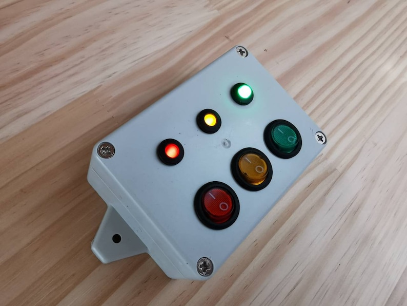 May include: A white plastic box with four buttons and three lights. The buttons are black with a red, yellow, and green light inside. The lights are red, yellow, and green.